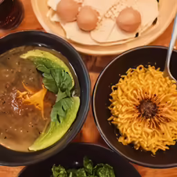 three bowls of different soups and some green vegetables