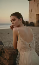 a woman stands next to a stone wall on a beach