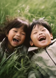 two little boys are laughing and laying in the grass,two young children laying in the grass and laughing
