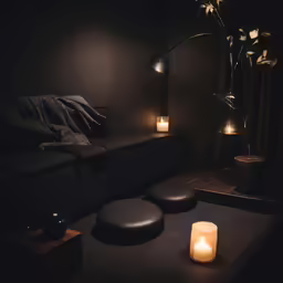 a small lighted candle and round stool in a black room