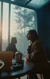 two people sit on a table with a tea pot and a coffee maker