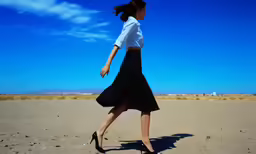 a woman in white shirt and black skirt walking across desert