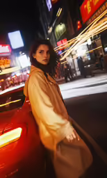 a woman leaning on the hood of a red car in a city at night