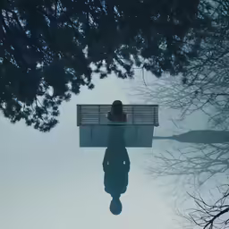 a reflection of someone sitting on a bench over water
