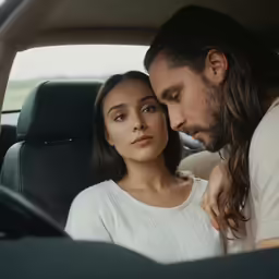 a couple cuddle in a car while looking at the camera