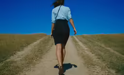 the back of a woman walking down a dirt road