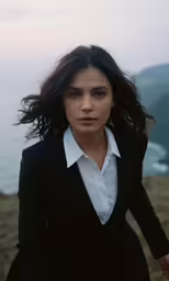 woman in black suit with wind blown hair, on top of rocky hillside