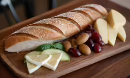this is a board with sliced bread, grapes, nuts, and cheese