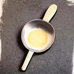 a wooden spoon sitting next to a bowl filled with yellow liquid