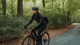a woman in black riding a bicycle on a wooded road
