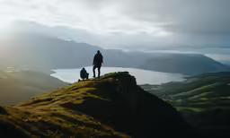 two people standing on top of a green mountain