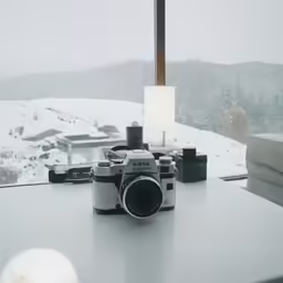 an old - fashioned camera sitting on a table in front of a snow - covered window