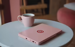 the pink laptop is next to a cup on a table