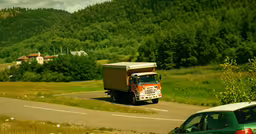 an orange truck traveling along a street with grass and trees in the background,the large truck is parked near a road