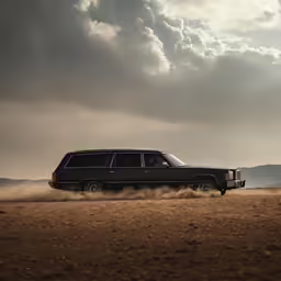 black vehicle moving in dirt and sand with clouds above