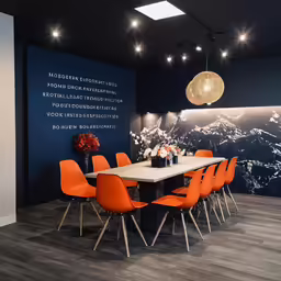 a modern dining area with orange chairs and a wall art