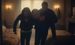 three people standing in the bedroom looking at a cellphone