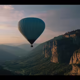 a large balloon flying in the air over a mountain range