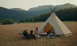 people sitting around a teepee in an open field