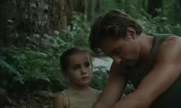a man and child sit in the woods near ferns