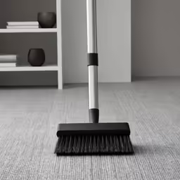 a broom laying on a carpet with a shelf in the background