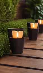 a number of candles sit on a deck in front of plants