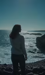 woman standing on the shore looking out at the ocean