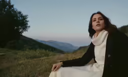 a woman sits on a hill and looks off to the left