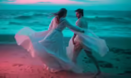 two people dressed in white are on the beach near the ocean