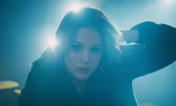 woman in dark outfit with a light shining behind her