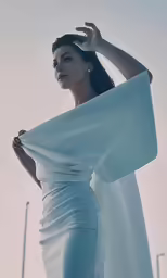 a woman is wearing a white dress and holding a large shaw