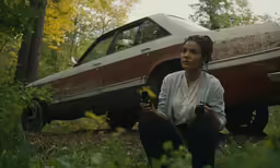 woman crouched in front of abandoned car in the forest