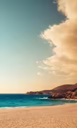 a surfer walks across a sandy beach with blue water