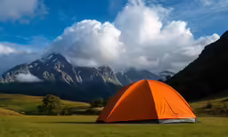 a tent pitched up in the grass with mountains in the background