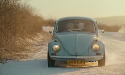 a vintage blue car driving on a snow covered road