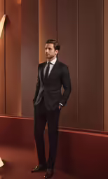 the man wearing a suit stands in front of brown colored wall