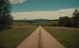 a dirt road runs through a large grassy field