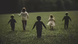four children playing in the grass outside with their hands in the air