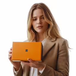 a woman holding up an orange box with an initial logo