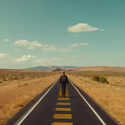 a person walking down the middle of a road next to a grassy field