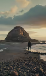 a man walking along a rocky beach in front of a mountain