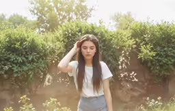 young woman holding her head, standing near shrubbery