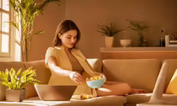 a woman wearing short shorts is sitting on a couch holding a bowl of food
