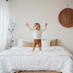 the little child is jumping on the bed