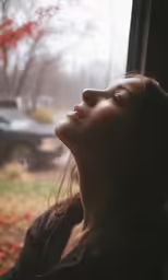 a woman looking out the window at leaves