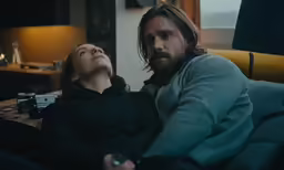 a man and a woman sitting on a couch with a remote in hand