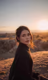 a young woman standing in the desert at sunset