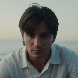 a man sitting in front of the ocean and staring at something