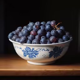 a bowl filled with blue grapes sitting on top of a table