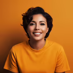 a woman smiling while standing against an orange wall